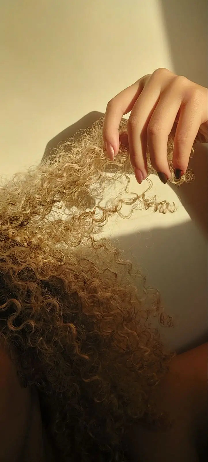 une main qui tiens des cheveux bouclé