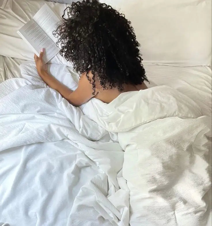 Femme sur un lit qui lit un livre sous la couverture, avec taie d'oreiller en soie SOIRENE Image
