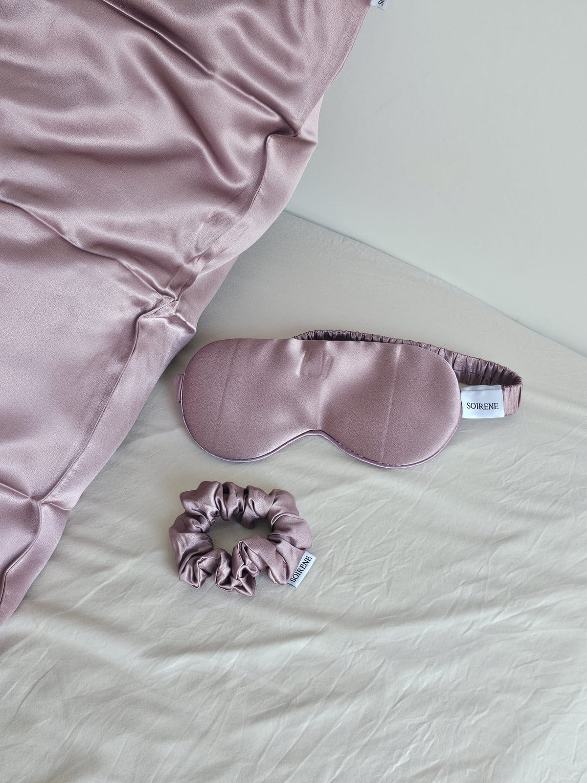 Ensemble d'accessoires de nuit SOIRENE en soie de mûrier mauve comprenant une taie d'oreiller, un masque de sommeil et un chouchou sur un lit