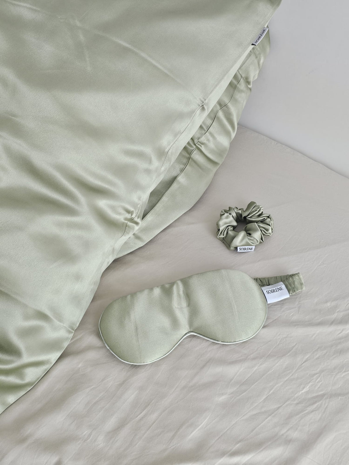Ensemble d'accessoires de nuit SOIRENE en soie de mûrier vert pistache comprenant une taie d'oreiller, un masque de sommeil et un chouchou sur un lit