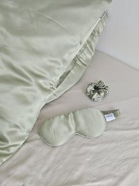 Ensemble d'accessoires de nuit SOIRENE en soie de mûrier vert pistache comprenant une taie d'oreiller, un masque de sommeil et un chouchou sur un lit