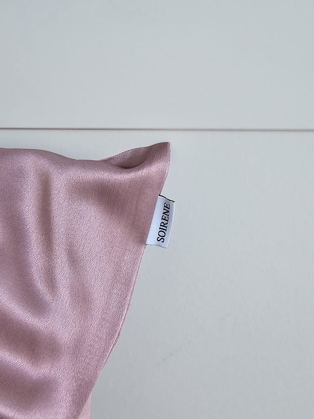 Gros plan détaillé montrant la texture satinée de la taie d'oreiller en soie de mûrier mauve SOIRENE et l'étiquette de marque avec le logo SOIRENE