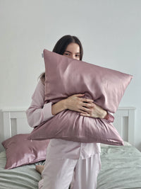 Femme souriante en pyjama rose tenant contre elle une taie d'oreiller en soie de mûrier mauve SOIRENE