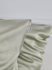 Gros plan sur une taie d'oreiller en soie de mûrier vert pistache SOIRENE montrant la couture soignée et l'étiquette de marque visible.